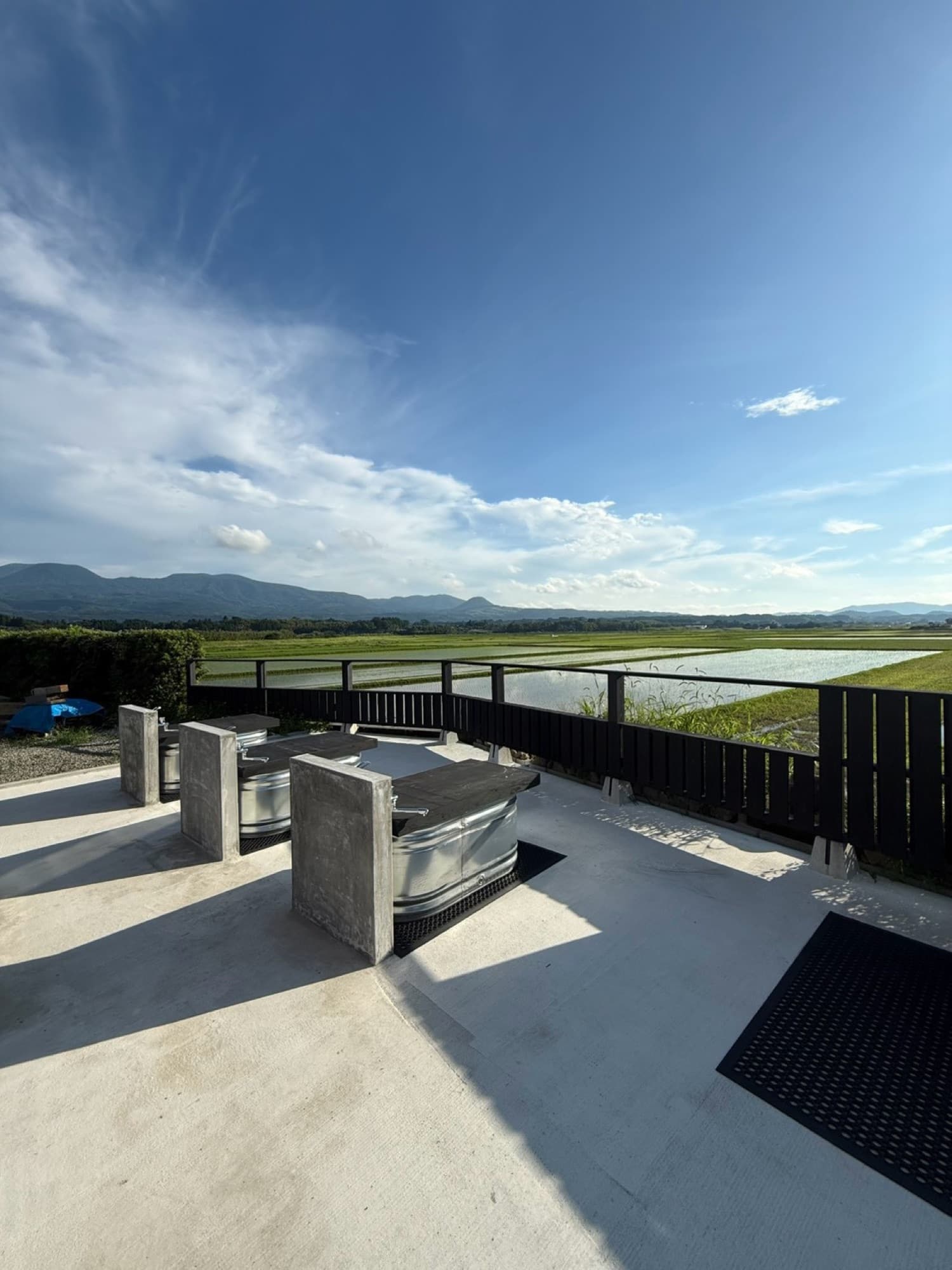 The outdoor terrace with galvanized cold-plunge tubs under an open sky, facing the rice fields